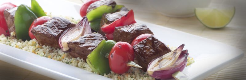 Onion, tomato, pepper, and beef kabobs on a bed of rice
