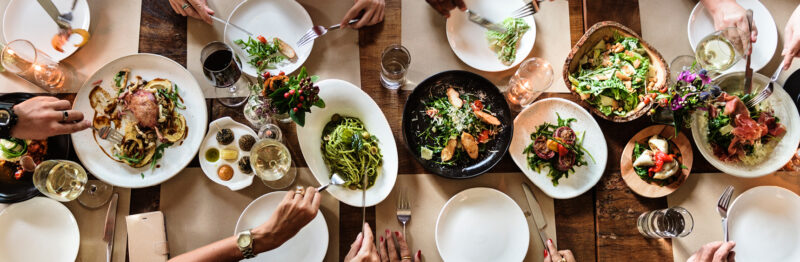 Overhead shot of a family style meal with hands serving food